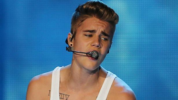 Justin Bieber singt mit einem Headset-Mikrofon vor einem blauen Hintergrund.