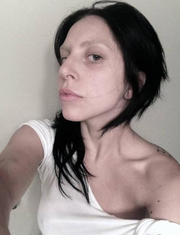 Lady Gaga mit dunklen Haaren und gebleichten Augenbrauen in einem weißen T-Shirt.