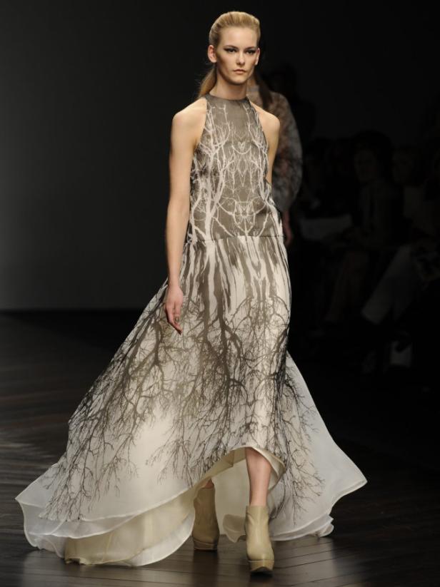 Eine Frau auf dem Laufsteg trägt ein langes, ärmelloses Kleid mit einem Baumzweigmuster.