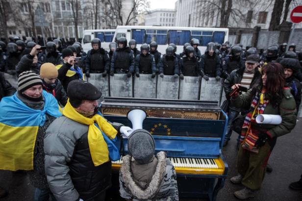 Vor einer Reihe von Polizisten steht ein blau-gelb bemaltes Klavier, umringt von Menschen.