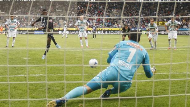 Ein Fußballspieler schießt einen Elfmeter, während der Torwart versucht, den Ball zu halten.