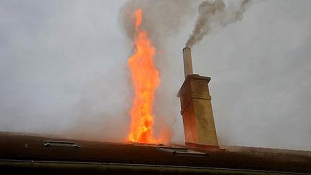 Flammen schlagen aus einem Dach neben einem Schornstein.