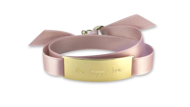 Ein zartrosa Armband mit einer goldenen Plakette, auf der „live, laugh, love“ steht.