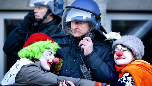 Polizisten in Schutzkleidung interagieren mit als Clowns verkleideten Demonstranten.