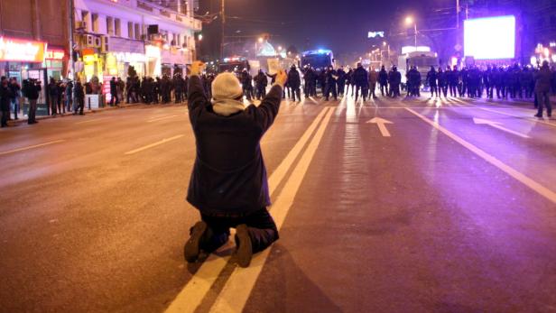 Ein Demonstrant kniet mit erhobenen Händen vor einer Reihe von Polizisten auf einer nächtlichen Straße.