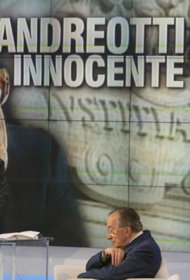 Giulio Andreotti sitzt vor einem Bildschirm mit der Aufschrift „Andreotti Innocente“.
