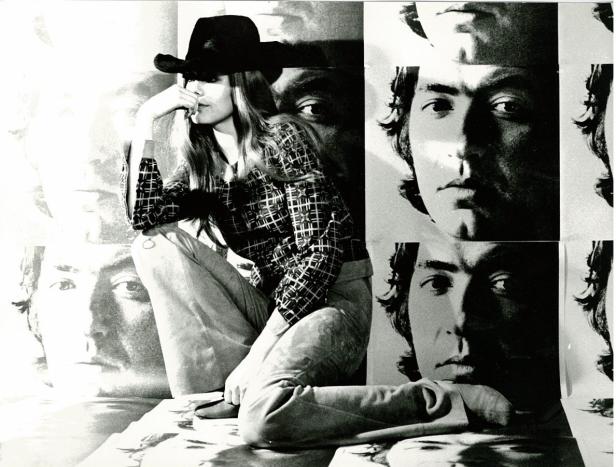 Eine Frau mit Hut posiert vor einem Hintergrund mit Porträts.