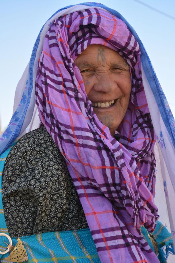 Eine lächelnde ältere Frau mit traditioneller Kopfbedeckung und Gesichtstattoos.