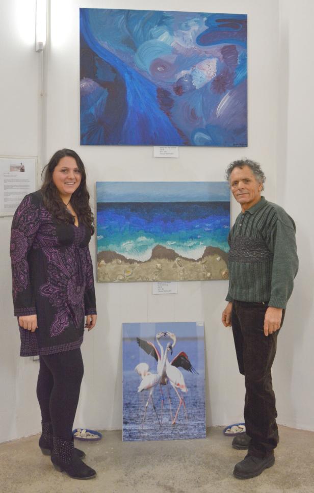 Eine Frau und ein Mann stehen in einer Kunstausstellung vor drei Bildern.