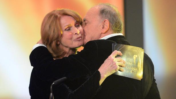 Senta Berger wird von einem Mann mit der Goldenen Kamera auf der Bühne umarmt.
