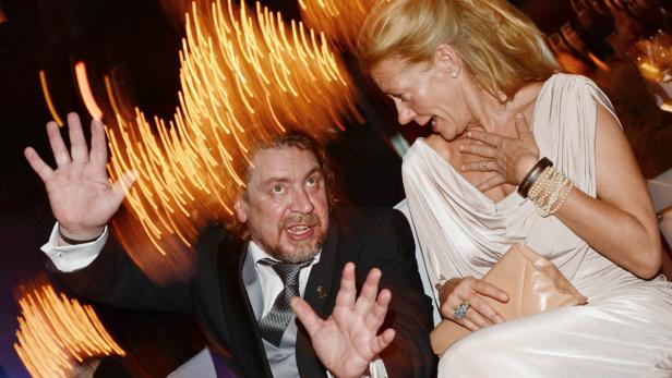 Ein Mann im Anzug gestikuliert aufgeregt, während eine Frau daneben überrascht wirkt.