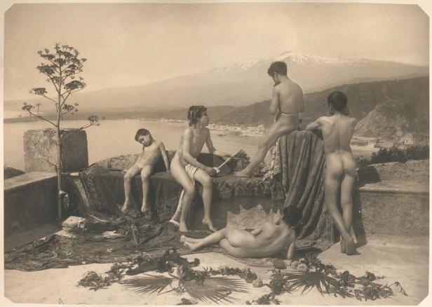 Eine Gruppe nackter junger Menschen posiert vor einer Landschaft mit einem Vulkan im Hintergrund.
