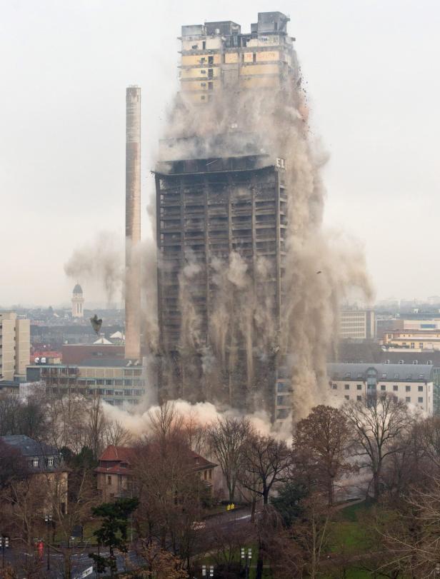 Ein Hochhaus wird gesprengt, Staub und Trümmer fliegen durch die Luft.