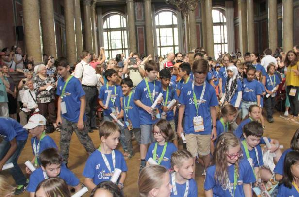 Eine Gruppe Kinder in blauen T-Shirts versammelt sich in einem großen Saal.