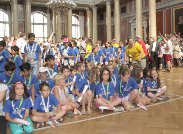 Eine große Gruppe Kinder sitzt auf dem Boden in einem großen Saal.
