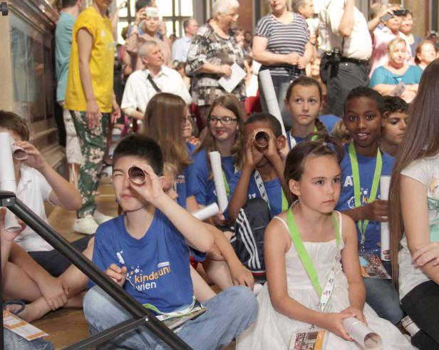 Eine Gruppe Kinder sitzt auf dem Boden und blickt durch Papierrollen.