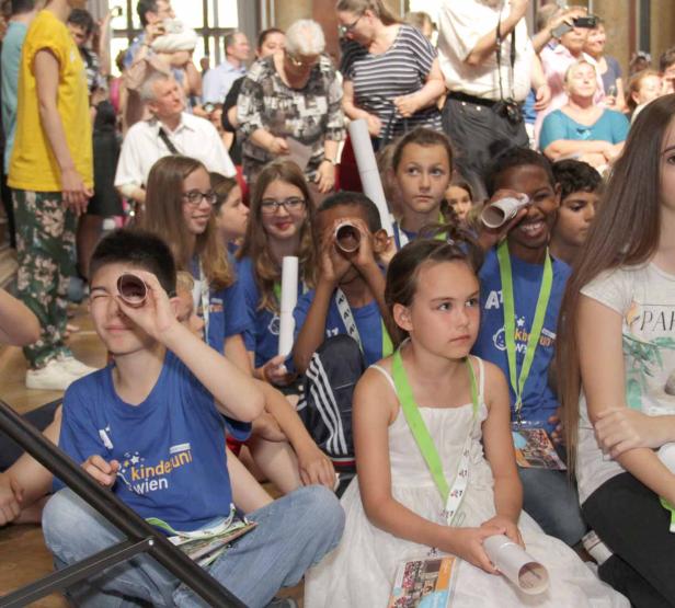 Eine Gruppe Kinder sitzt auf dem Boden und schaut durch Papierrollen.