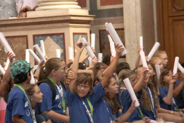 Eine Gruppe Kinder hält Papierrollen in die Höhe.