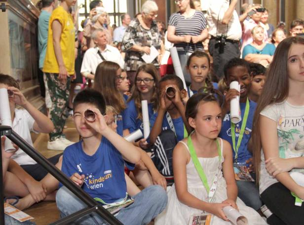 Eine Gruppe Kinder sitzt auf dem Boden und schaut durch Papierrollen.
