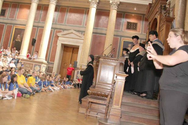Eine Gruppe von Kindern sitzt in einer Aula, während eine Zeremonie stattfindet.