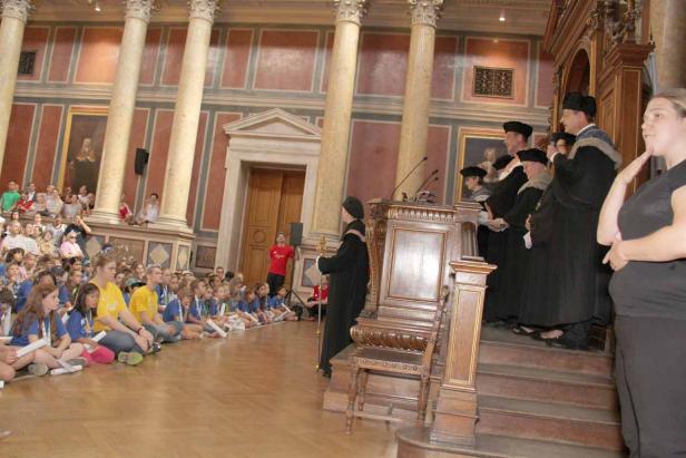 Eine Gruppe von Kindern sitzt auf dem Boden, während eine akademische Zeremonie stattfindet.