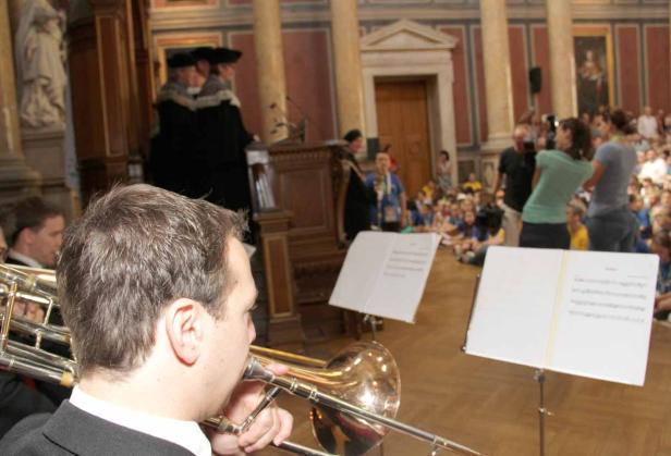 Ein Mann spielt Posaune vor einem Publikum in einem großen Saal.