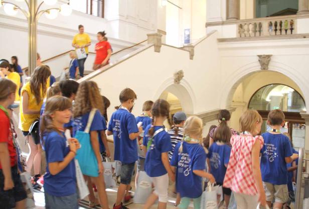 Eine Gruppe von Kindern in blauen T-Shirts geht eine Treppe in einem Gebäude hinauf.