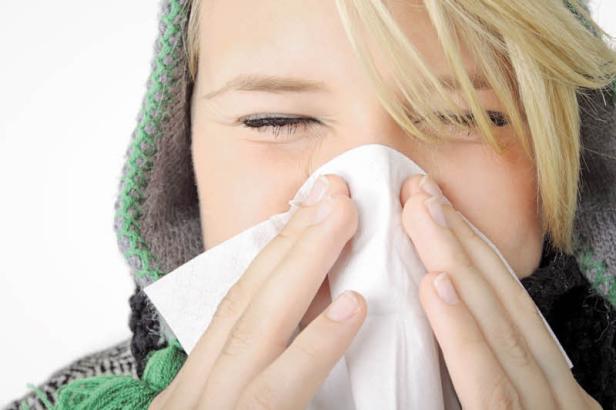Eine Frau mit blonden Haaren putzt sich die Nase mit einem Papiertuch.