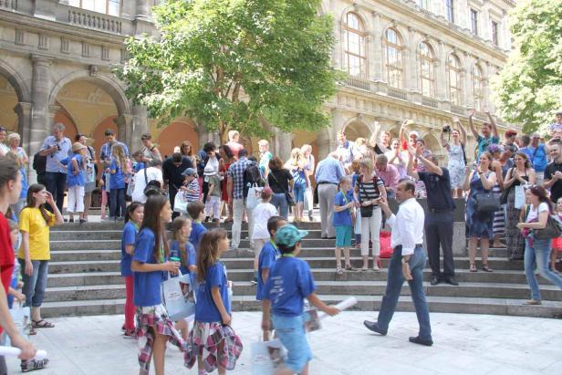 Eine Gruppe Kinder und Erwachsene steht auf den Stufen vor einem Gebäude.