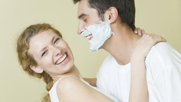 Eine lachende Frau umarmt einen Mann mit Rasierschaum im Gesicht.