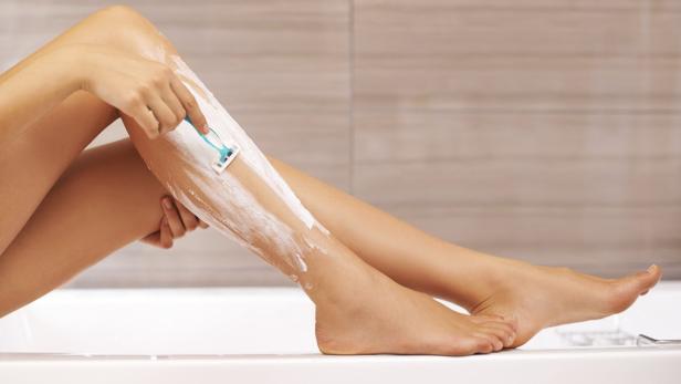 Eine Frau rasiert sich im Badezimmer die Beine mit Rasierschaum und einem Rasierer.