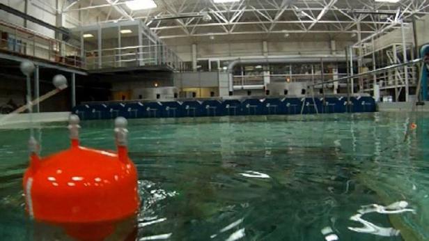 Ein roter Schwimmkörper treibt in einem großen Wasserbecken in einer Halle.