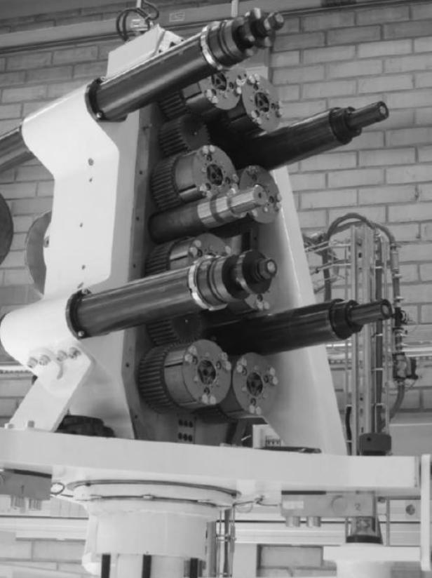 Eine komplexe Maschine mit mehreren Walzen und Zahnrädern in einer Fabrikhalle.