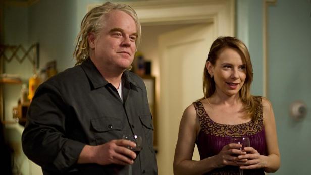 Philip Seymour Hoffman und Amy Ryan halten Weingläser in einem Innenraum.