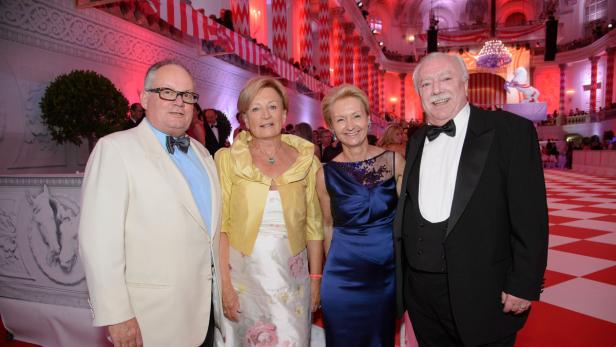 Vier Personen posieren auf einem Ball in festlicher Kleidung vor roter Dekoration.