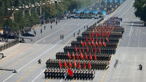 Eine Militärparade mit Soldaten und Militärfahrzeugen auf einer breiten Straße.