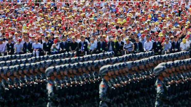 Eine Militärparade mit Soldaten in Uniform vor einer Zuschauermenge mit bunten Hüten.