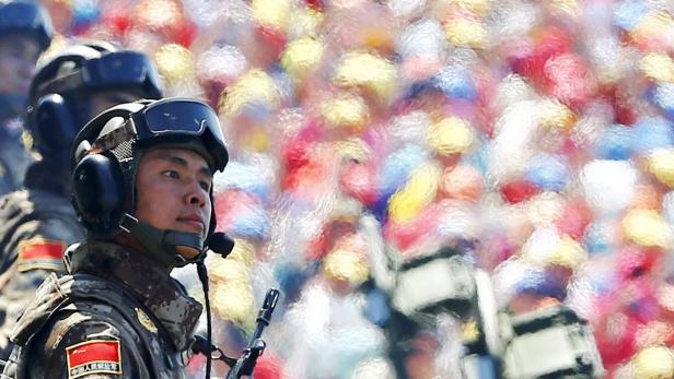 Ein chinesischer Soldat mit Helm und Gewehr vor einer Menschenmenge.
