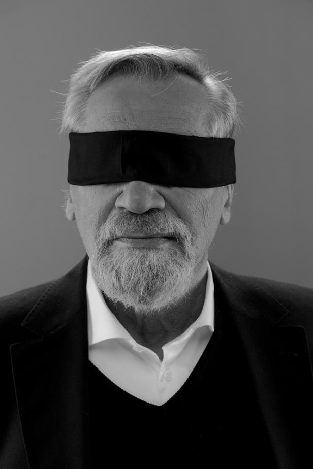Ein Mann mit grauen Haaren und Bart trägt eine schwarze Augenbinde.