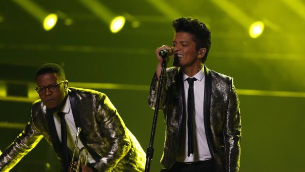 Bruno Mars singt mit einem Bandmitglied im Hintergrund auf der Bühne.