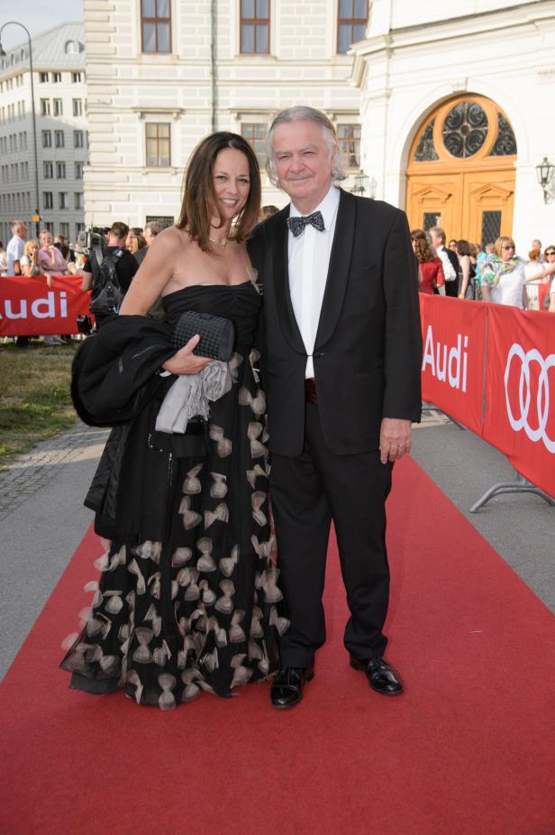 Ein Mann im Smoking und eine Frau im Abendkleid posieren auf einem roten Teppich.
