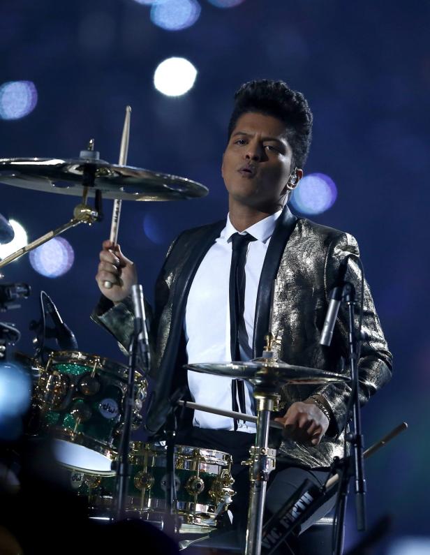 Bruno Mars spielt Schlagzeug in einem goldenen Blazer.