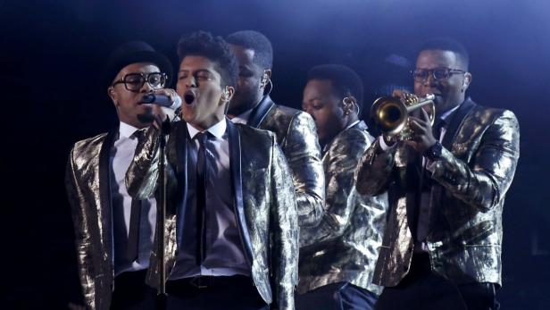 Bruno Mars und seine Band treten in glitzernden Anzügen auf einer Bühne auf.