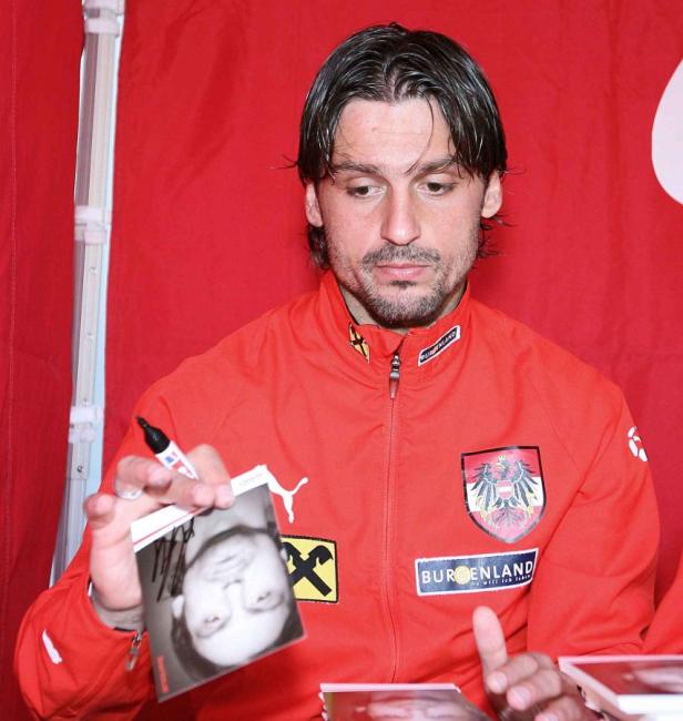Ein Mann in roter Jacke signiert ein Foto.