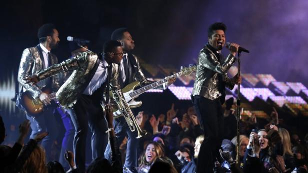 Eine Band tritt in goldenen Jacken vor einem begeisterten Publikum auf.