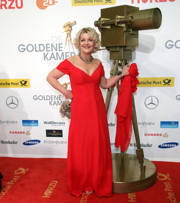 Eine Frau in einem roten Kleid posiert neben einer goldenen Kamera für „Die Goldene Kamera“.