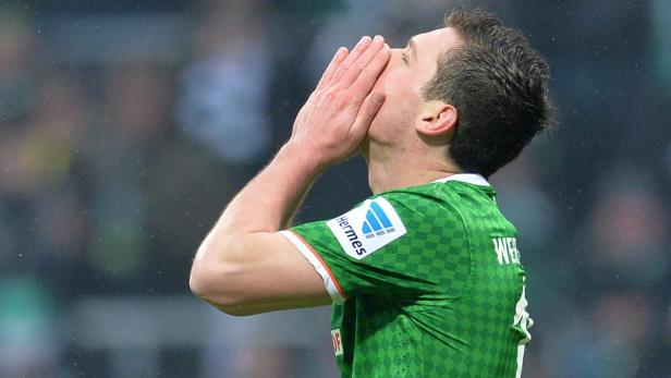 Ein Fußballspieler in einem grünen Trikot hält seine Hände vor sein Gesicht.