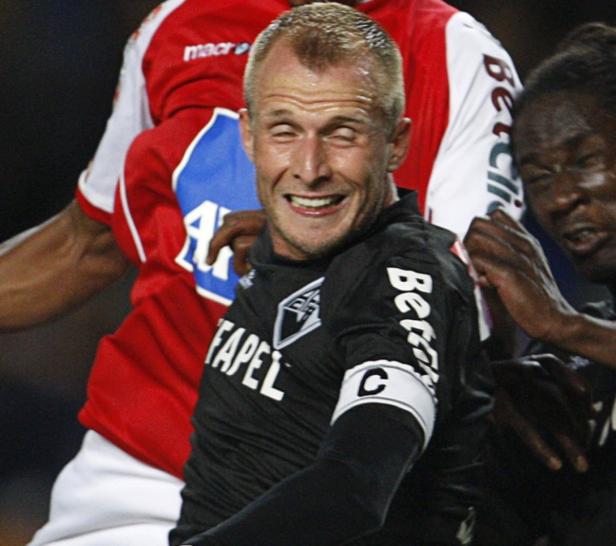Ein lachender Fußballspieler mit Kapitänsbinde im Spiel.