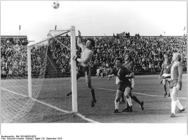 Ein Torwart springt, um einen Fußball vor einem vollen Stadion abzuwehren.