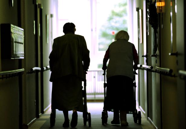 Zwei ältere Frauen gehen mit Rollatoren einen Flur entlang.